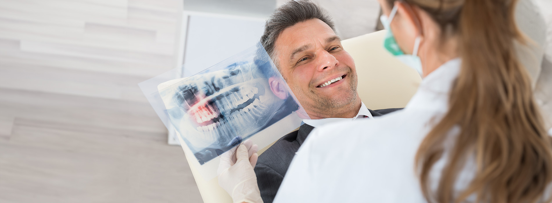 A person is seated in a dental chair, receiving care from a dental professional who stands behind them.