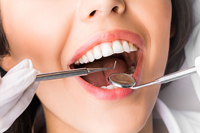 A person with a wide smile, wearing white gloves and holding a toothbrush in their mouth, while another person is seen from behind, wearing a face mask.